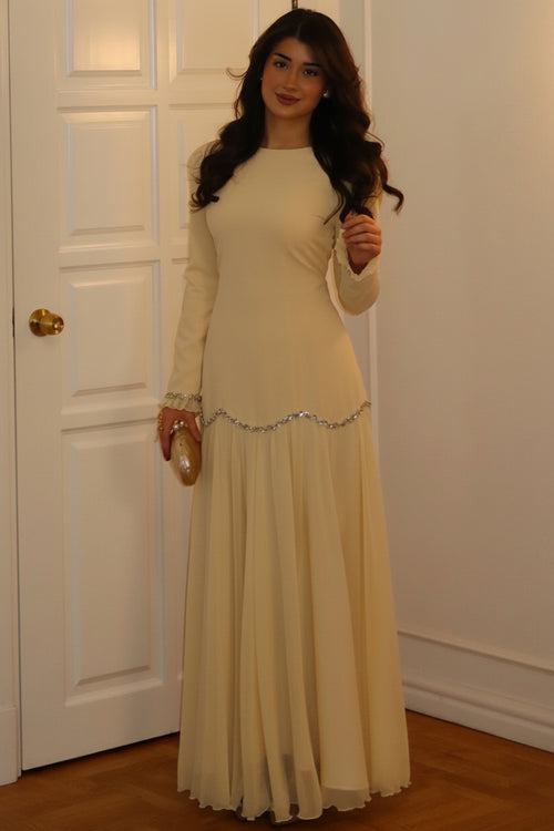 Woman in a long beige dress standing in a room with a white door.